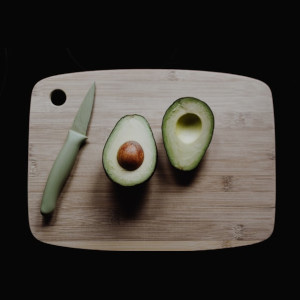 haas avocado sliced in two beside a knife sititing on a cutting board