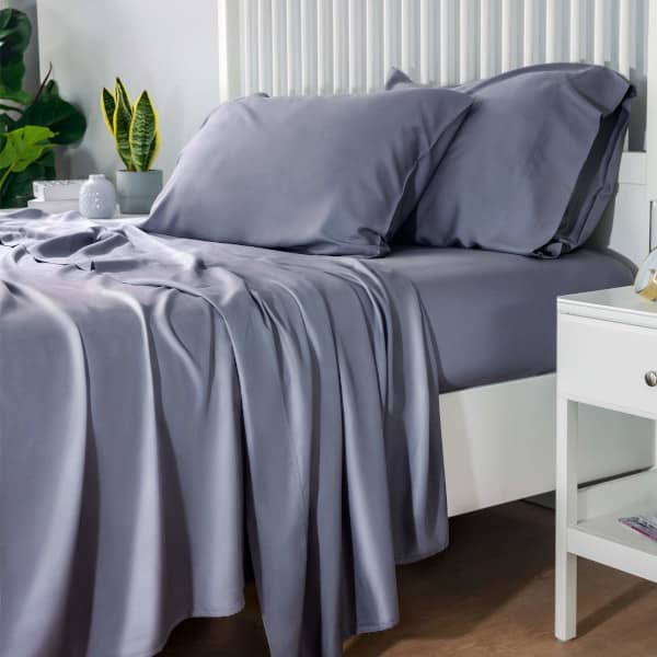 dark blue bamboo sheets and pillow case on a bed with a white frame between two night stands and some plants